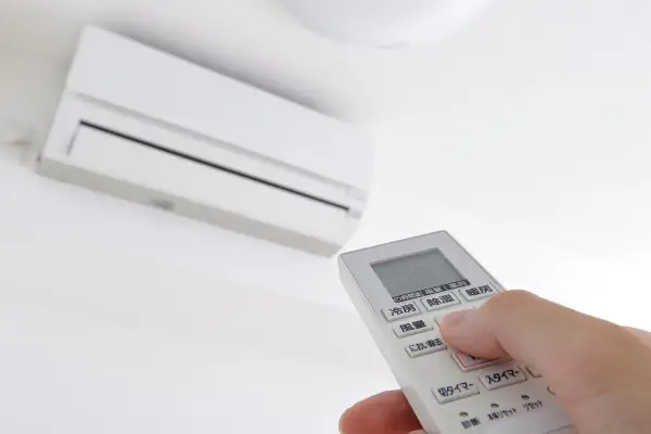 Mano ajustando el **timer on aire acondicionado** con el control remoto. El aire acondicionado blanco está montado en la pared.