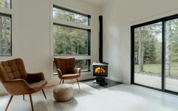 Un poêle à granule appartement, avec deux fauteuils en cuir marron et une vue sur la forêt.