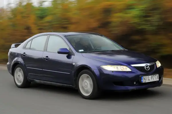 Granatowa Mazda 6 GG jedzie po drodze, za nią rozmyty krajobraz jesiennych drzew.