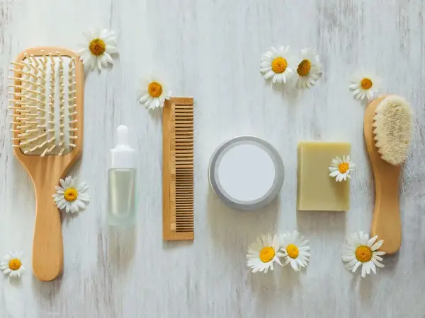 Cepillo, peine, jabón y serum de cuidado personal, todo cruelty free, rodeado de margaritas sobre fondo de madera.