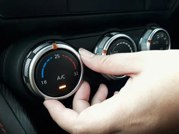 Dłoń reguluje pokrętłem temperaturę klimatyzacji w samochodzie, ustawiając ją na 25 stopni.