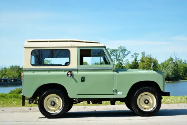 Land Rover Santana verde y crema, listo para una aventura todoterreno junto a un lago.