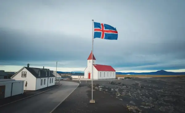 Islandia praca: biały kościół z czerwoną wieżą i flagą Islandii na tle pochmurnego nieba.