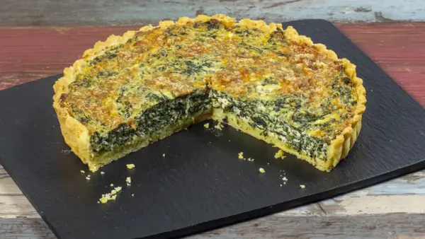 Una fetta di torta salata ricotta e spinaci, con crosta dorata e ripieno cremoso, servita su una lavagna scura.