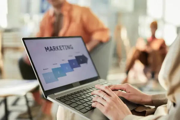 Osoba pracuje na laptopie z prezentacją "MARKETING". Widoczne etapy: Research, Analysis, Sales. Idealne do studiów zarządzanie i marketing.