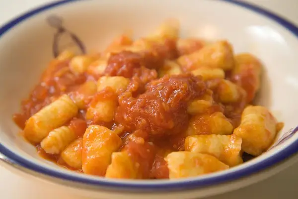 Pyszne gnocchi alla sorrentina w sosie pomidorowym, podane w białej misce z niebieskim rantem.