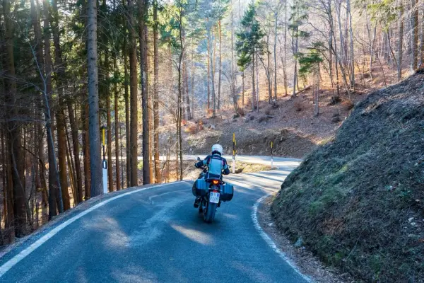 Motociclista su strada tortuosa tra i boschi, un'avventura **rund um den Gardasee**.