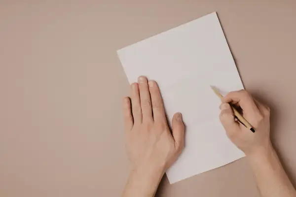 Ręce piszą list motywacyjny po angielsku na białej kartce.