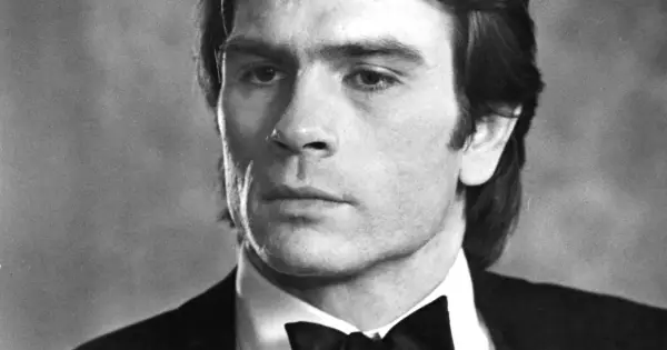 Młody Tommy Lee Jones w czarnym smokingu z muszką, zamyślony.