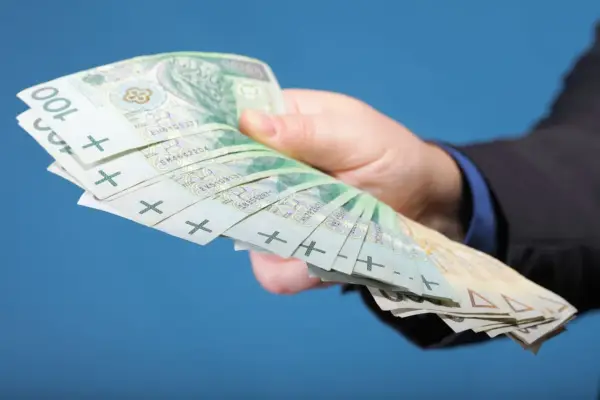 Dłoń w garniturze trzyma plik banknotów 100 zł. Zastanawiasz się, ile zarabiają gwiazdy seriali?