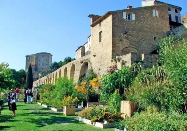 Jardin luxuriant devant le **château de Lauris**, avec ses murs de pierre et ses arches médiévales.