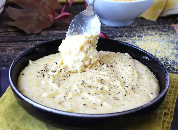 Une cuillère sert une portion généreuse de polenta crémeuse, assaisonnée de poivre noir, dans un bol. Une recette polenta réconfortante.