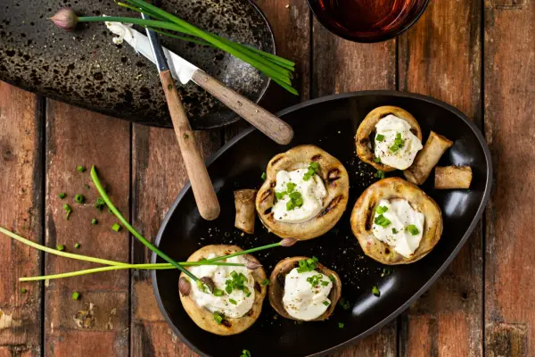 Champignons au barbecue farcis de fromage crémeux et garnis de ciboule fraîche. Un délice simple pour un repas estival.