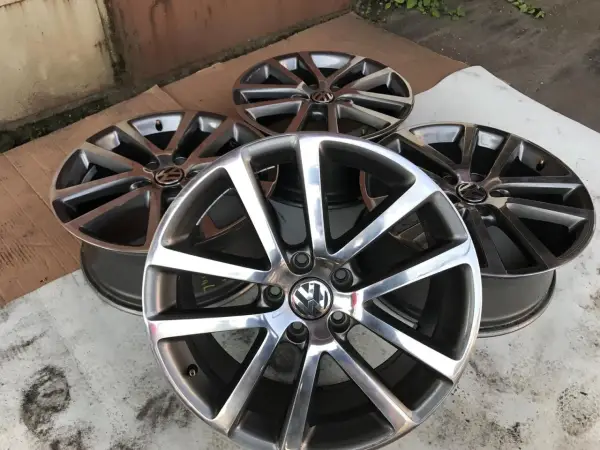 Cztery aluminiowe felgi Volkswagen z logo, ułożone na ziemi.