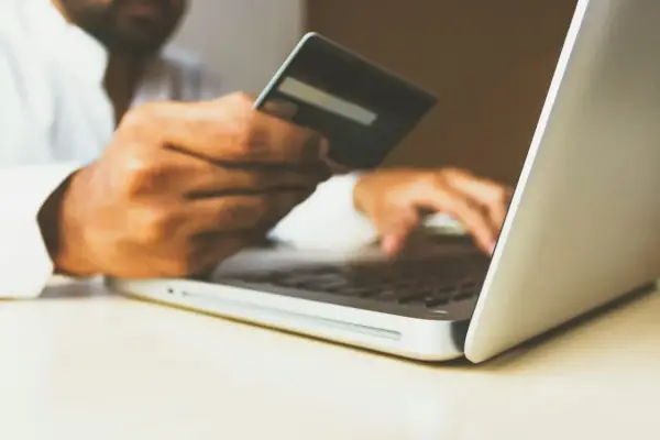 Homme utilisant une carte bancaire sur un ordinateur portable pour configurer un virement automatique de loyer avec son RIB.