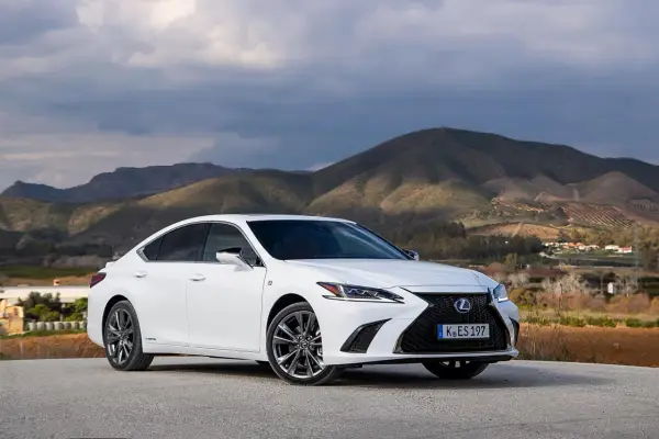 Biały Lexus ES 300h zaparkowany na tle górskiego krajobrazu. Elegancki sedan prezentuje się okazale na tle natury.