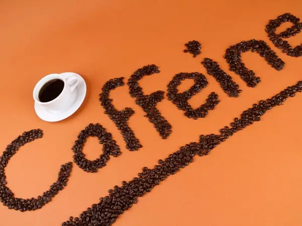 Ziarna kawy ułożone w napis "caffeine" obok filiżanki kawy. Zastanawiasz się, ile kofeiny ma łyżeczka kawy mielonej?