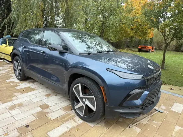 Nowy, granatowy Fisker SUV stoi na wybrukowanym podjeździe. W tle żółty i pomarańczowy samochód.