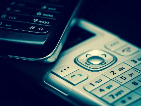 Zbliżenie na klawiatury dwóch telefonów komórkowych, jeden czarny, drugi srebrny.