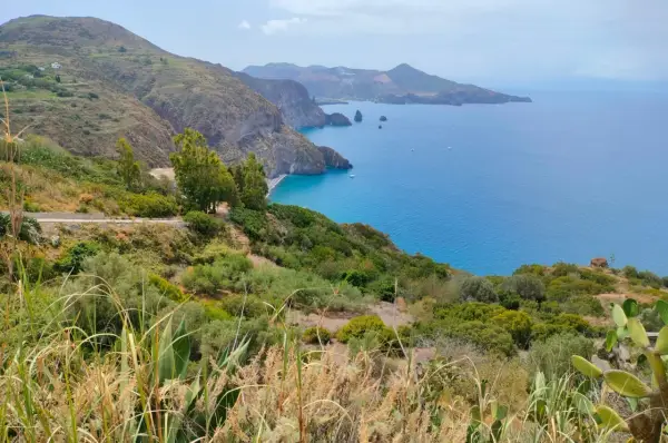 Panoramica mozzafiato per capire come visitare le Isole Eolie: costa verdeggiante, mare blu intenso e isole vulcaniche all'orizzonte.