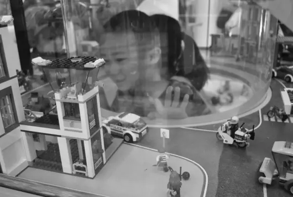 Bambina osserva con stupore un **reportage fotografico** di idee con costruzioni Lego: un commissariato, auto della polizia e personaggi in azione.
