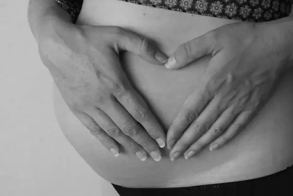 Dłonie tworzą serce na brzuchu ciężarnej. Intensywne ruchy dziecka mogą być sygnałem niedotlenienia.
