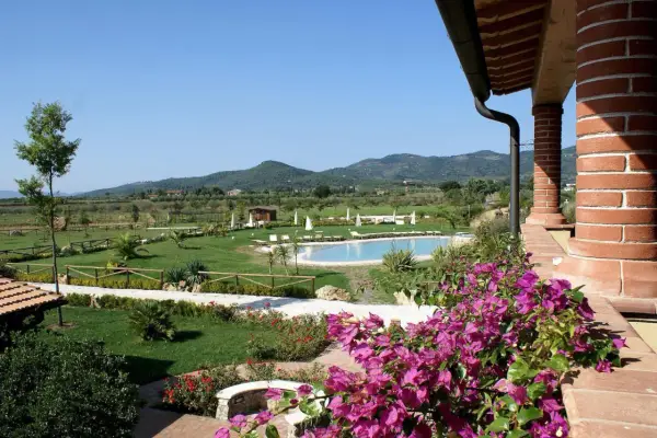 Un angolo di campagna toscana lungo il mare, con piscina, giardini curati e colline verdi all'orizzonte.