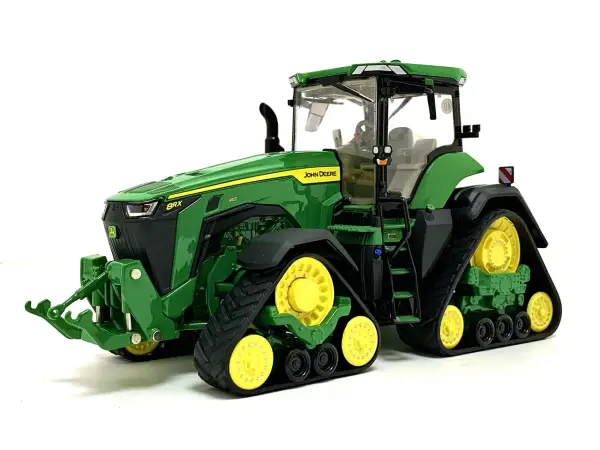 Zielony mini traktor John Deere z żółtymi kołami i gąsienicami, gotowy do pracy na farmie.