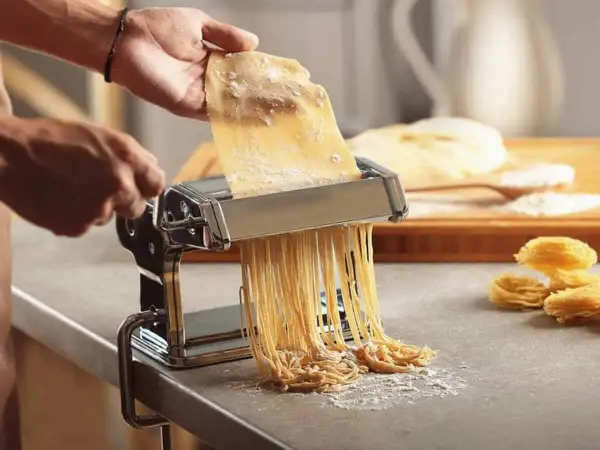Préparation d'une recette de pâte italienne gastronomique. Une machine à pâtes produit des spaghettis frais, prêts à être cuisinés.