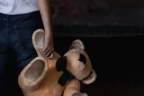 Main d'enfant tenant un ours en peluche. Un signalement enfance en danger en ligne peut aider.