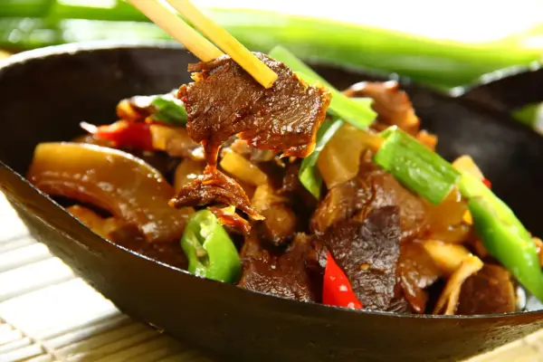 Chopsticks podnoszą kawałek aromatycznej wołowiny po chińsku z miski pełnej pysznego dania z warzywami.