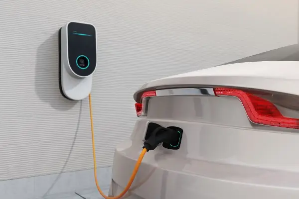 Nowoczesna stacja ładowania samochodów elektrycznych podłączona do białego auta. Sprawdź, jaka jest stacja ładowania samochodów elektrycznych cena.