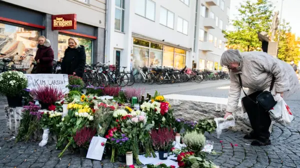 En kvinna lägger blommor vid en minnesplats för Kim Larsen. Många blommor och ljus.