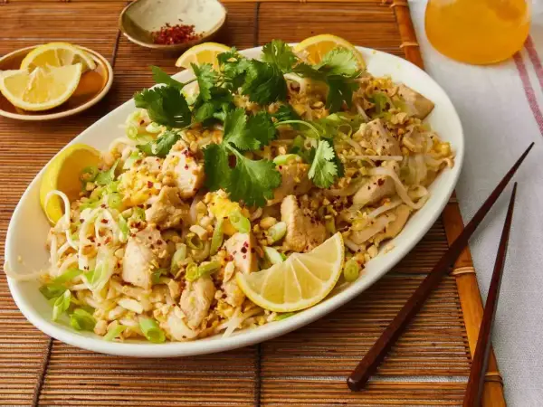 Pyszne pad thai co to? Danie z kurczakiem, makaronem ryżowym, orzeszkami ziemnymi i świeżą kolendrą, podane z cytryną.