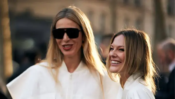 Dos mujeres sonríen, una con gafas de sol y pelo liso rubio, la otra con pelo liso castaño.