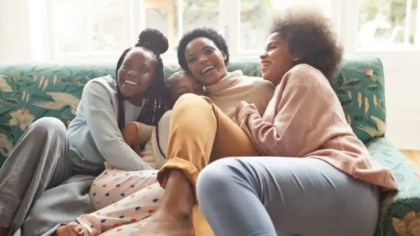 Une famille rit aux éclats sur un canapé. L'ainé de la famille, la plus grande, est au centre, entourée de ses sœurs.