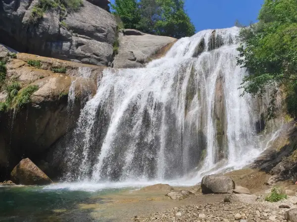 Cascada del Moli, con agua cayendo sobre rocas y vegetación exuberante, formando una piscina natural.
