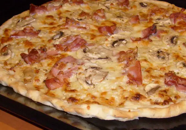 Pyszna pizza carbonara z chrupiącym boczkiem, pieczarkami i ciągnącym się serem. Idealna na szybki obiad.