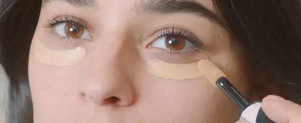 Aplicando corrector para disimular las ojeras antes o después del maquillaje.
