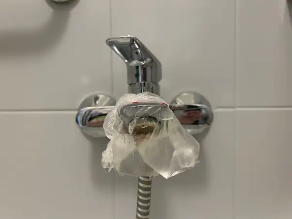 Krople wody spływają z baterii, na której zawiązano woreczek. To metoda, jak wyczyścić sitko w baterii kuchennej.