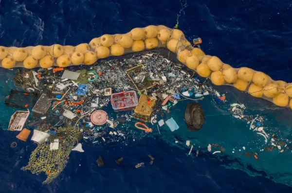 Sieć rybacka z żółtymi bojami zbiera dryfujące śmieci na oceanie, w tym plastik i oponę.
