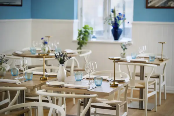 Vackert dukade bord med blåa glas och blommor i vaser, redo för gäster på en av restaurangerna i Skagen.