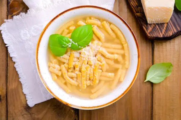 Piatto di passatelli in brodo, un classico dei piatti romagnoli, guarnito con basilico fresco e parmigiano.