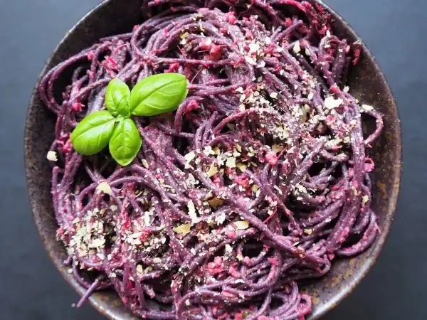 Fioletowy makaron z pesto ze słoika, posypany orzechami i udekorowany listkiem bazylii.