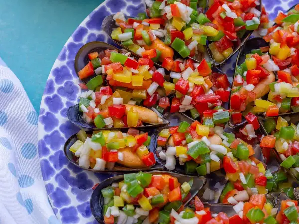 Mejillones a la vinagreta, cubiertos con una colorida mezcla de pimientos y cebolla picados. Un plato fresco y vibrante.