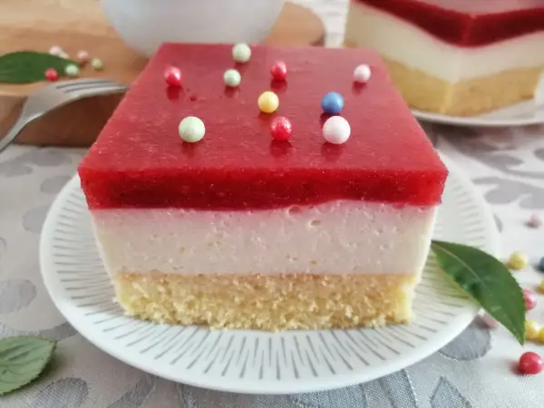 Pyszna żelka truskawkowa z mrożonych truskawek, z kremową warstwą i biszkoptem, ozdobiona kolorowymi kuleczkami.