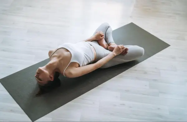 Kobieta w pozycji supta baddha konasana na macie do jogi, relaksująca biodra i pachwiny.