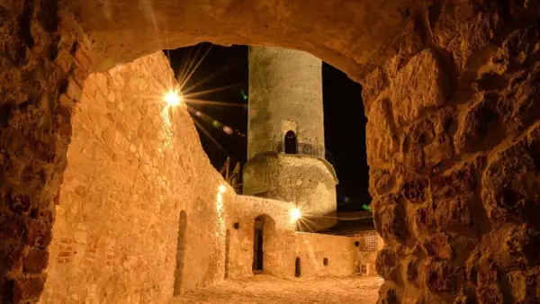 Kamienna wieża i mury zamku w Iłży nocą, oświetlone ciepłym blaskiem lamp.