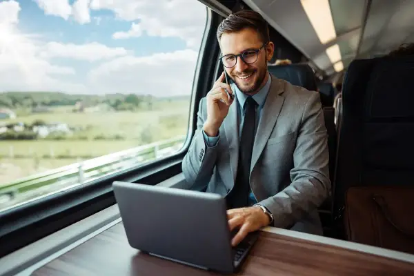 Biznesmen w garniturze rozmawia przez telefon i pracuje na laptopie w pociągu. Planuje swoją dietę zagraniczną w Niemczech.