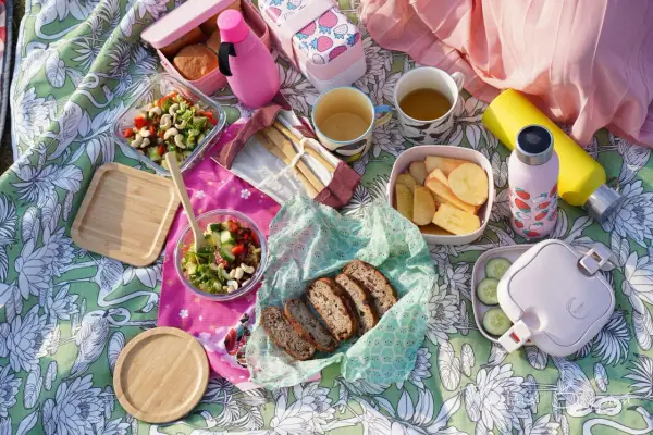 Piknikowy koc z jedzeniem: sałatki, chleb, owoce, napoje i bambuowe sztućce.